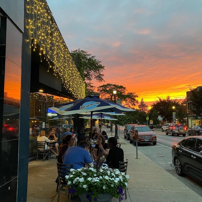 people sitting at outdoor restaurant tables on sidewalk on main street during sunset