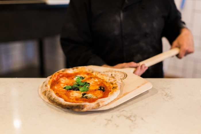 man holding a wooden pizza paddle with a pizza on it