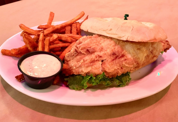 battered fish sandwich on brioche bun with lettuce served with sweet potato fries and sauce