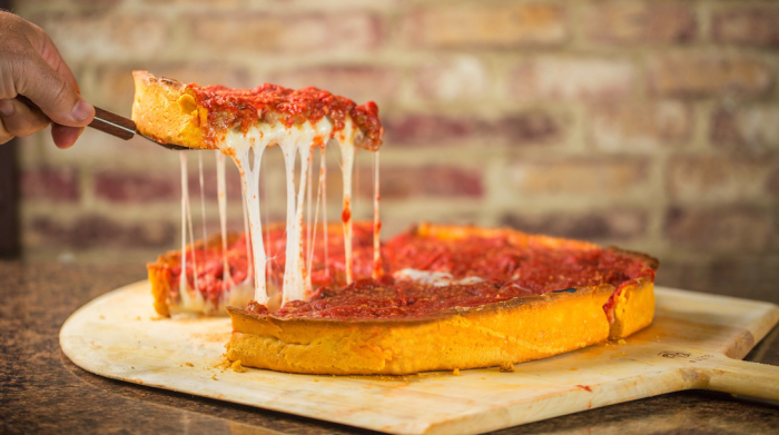 hand lifting a slice of deepdish pizza with gooey cheese from the pizza