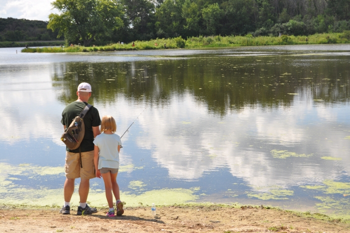 father and daughter standing fishing from bank into water