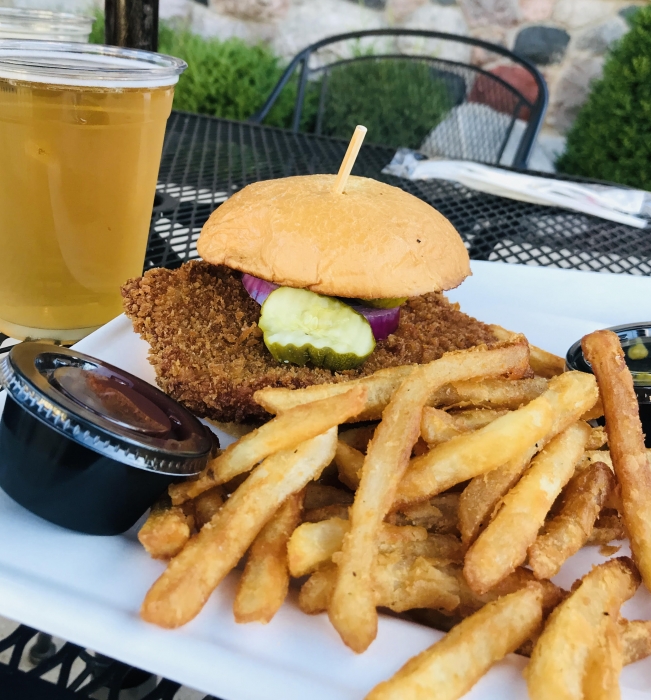 battered fish sandwich on bun with pickle and onion served with fries and glass of beer