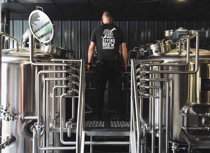white male brewer in black shirt standing by brewing equipment