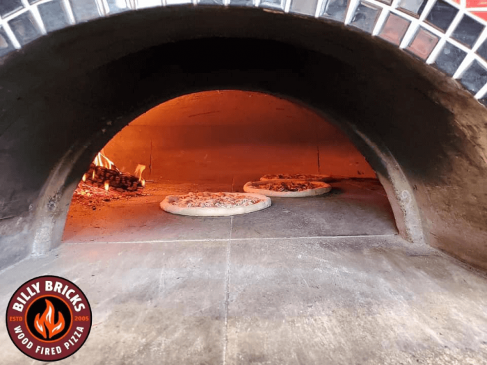 two pizzas cooking inside a woodfired brick oven