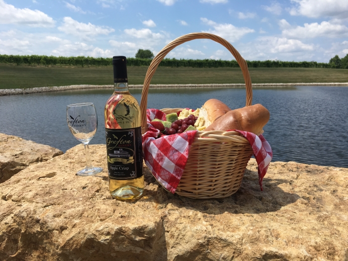 picnic basket with wine sittting on a rock with water in the background