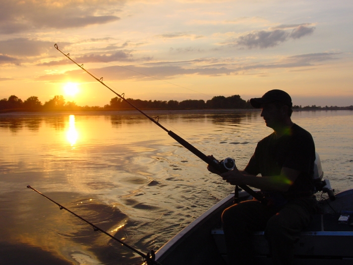 man seated in boat fishing during sunset