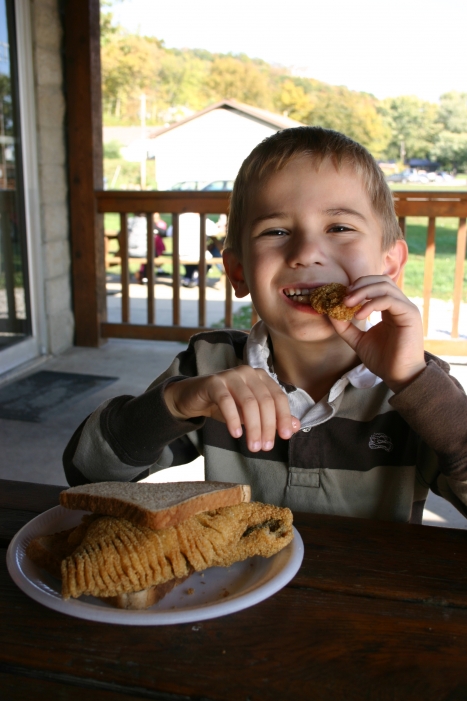 young boy eating battered catfish fillet sandwich on wheat bread at picnic table