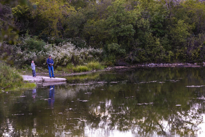 father and son standing on wooded bank fishing in river