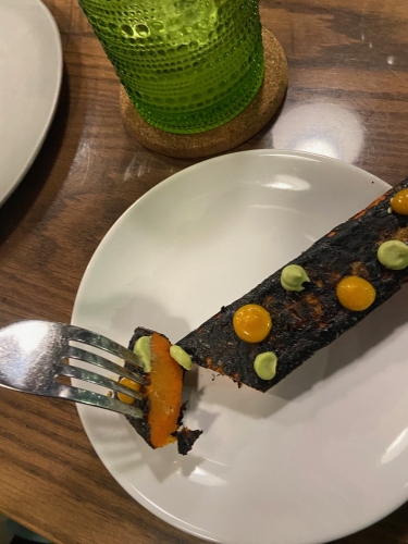 Rectangle shaped blackened carrot with dollops of orange and green sauce. Fork poised above white plate.