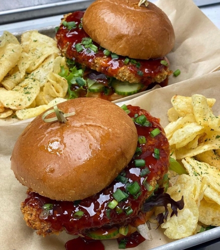 Two nearly identical burger-type sandwiche with brown meat and red sauce, nestled with yellow potato chips