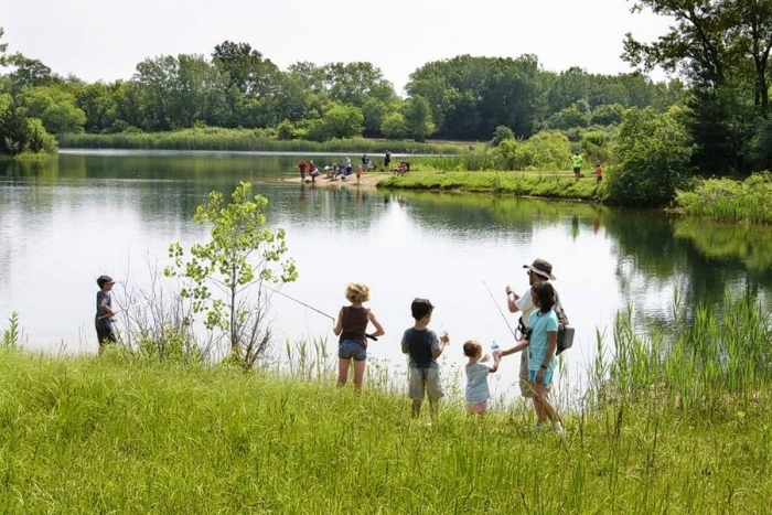 5 kids standing on grassy bank waiting to fish while man baits a hook for one of them