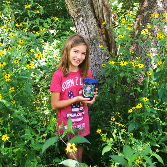 girl standing by tree with geocache container surrounded by yellow flowers