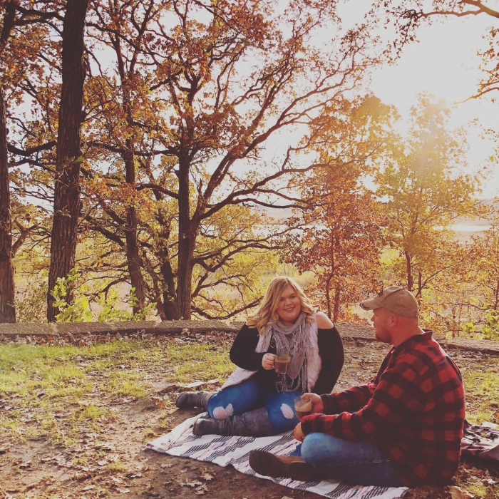 man and woman couple sitting on picnic blanket in the fall drinking beer from glass mugs