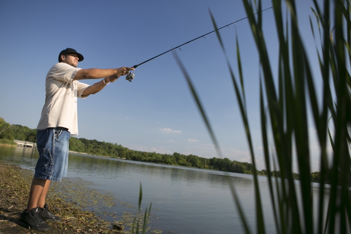 man standing on bank of lake fishing on sunny day
