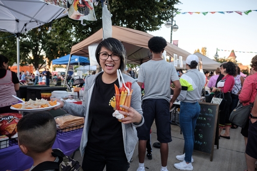 hispanic female holding icecream treat and plate of food at outdoor street market