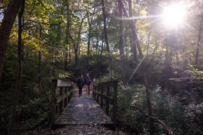 young man woman couple walking on path in the woods on sunny early fall day