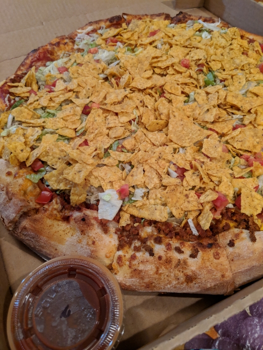 taco pizza topped with sausage, cheese, lettuce, tomatoes, crushed doritos