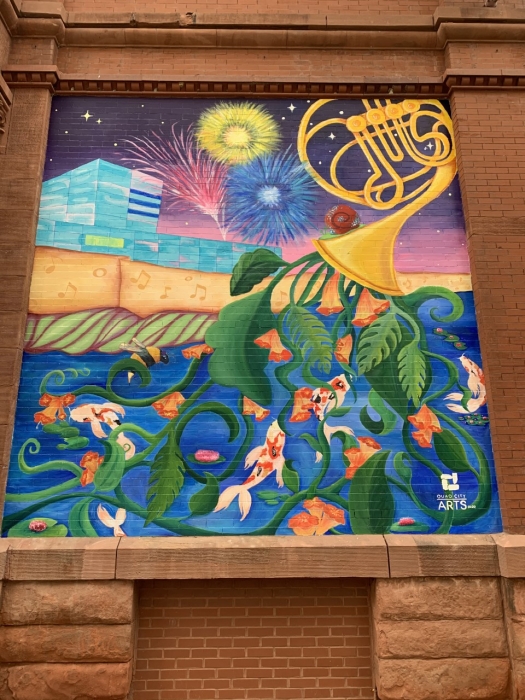painted mural by artist with a french horn instrument spilling plants out of its horn
