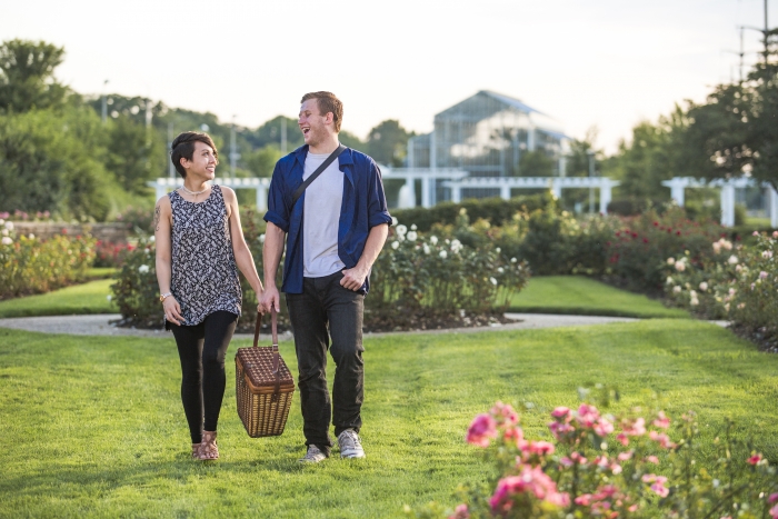 man and woman couple walking with picnic basket in a rose garden