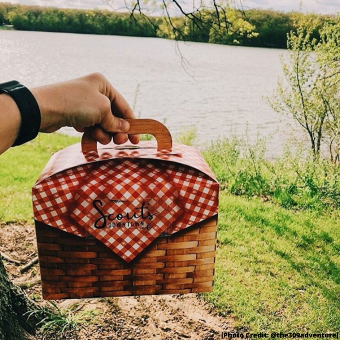 male hand holding a picnic basket with river in the background