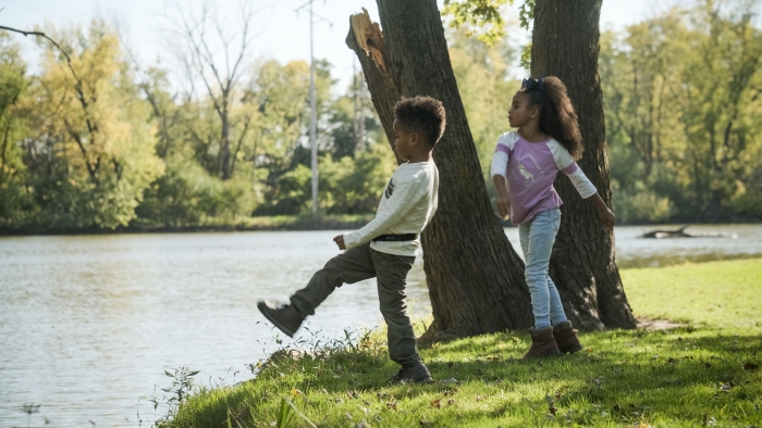 two younger kids playing outside by a forest stream