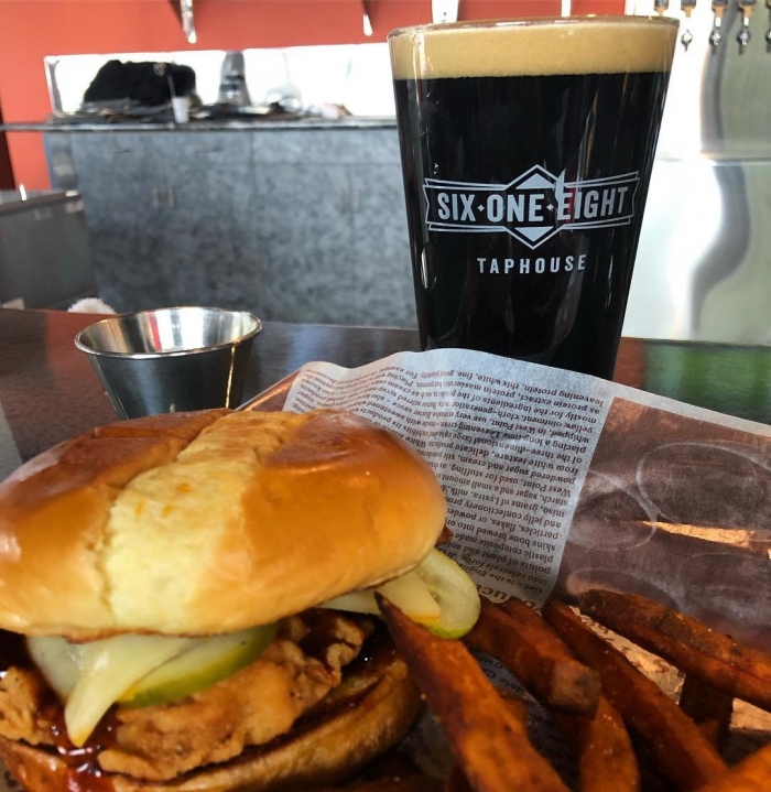 glass of dark beer with some foam with a sandwich and fries