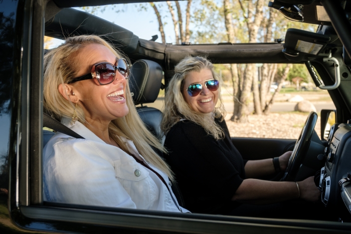 two blonde women in sunglasses in the front seats of a Jeep with an open top