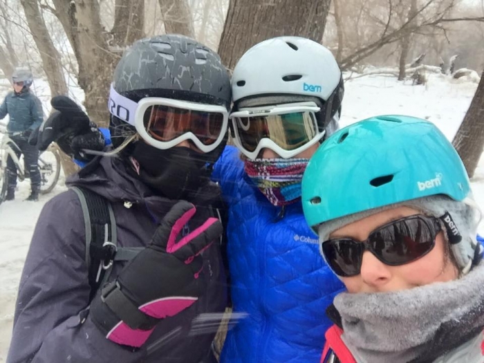 3 women posing together in helmets and goggles outside in winter forest