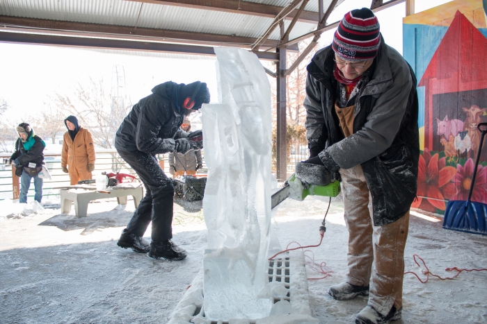 2 guys working on carving ice sculptures outside winter