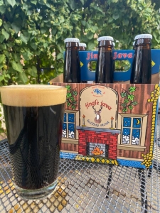 6 pack of dark beer bottles on a patio table with a glass of dark beer