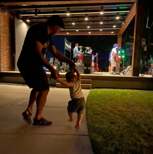 toddler son dancing near dad with band playing in background outside