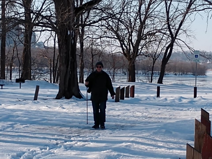 woman bundled up walking on winter snow-covered path with walking poles