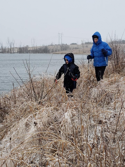 mom and son bundled up winter walking by water in tall grass